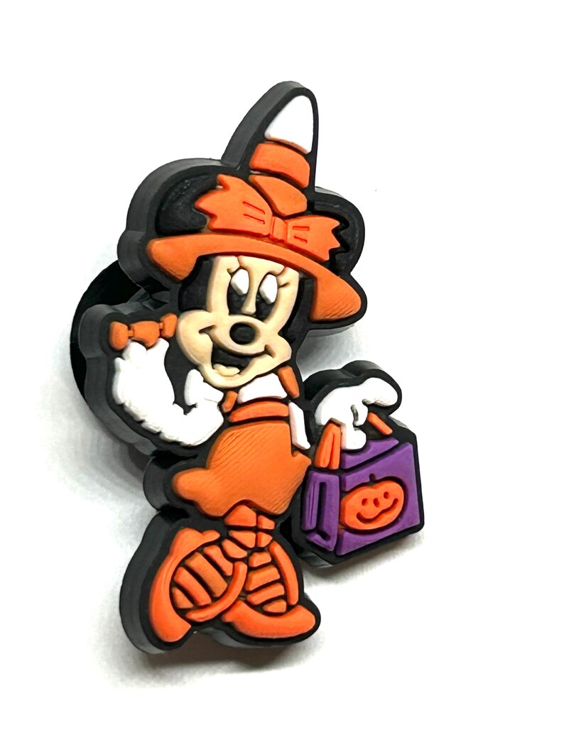 K&ouml;nnte beinhalten: Ein Halloween-Themen-Minnie-Mouse-Charm in Schwarz, Orange, Wei&szlig; und Lila. Minnie ist als Hexe verkleidet, tr&auml;gt einen Hut und h&auml;lt eine S&uuml;&szlig;igkeitent&uuml;te mit einem K&uuml;rbisgesicht. Der Charm hat einen schwarzen Rand.
