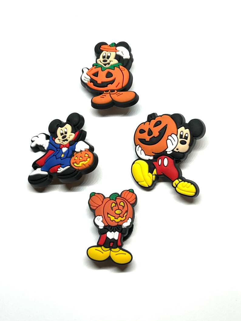 K&ouml;nnte beinhalten: Vier Halloween-Schuhanh&auml;nger mit Mickey Mouse-Charakteren. Jeder Anh&auml;nger zeigt Mickey in verschiedenen Kost&uuml;men, darunter ein Vampir und eine Jack-o'-Laterne. Die Anh&auml;nger sind haupts&auml;chlich schwarz, orange, rot, blau und gelb.