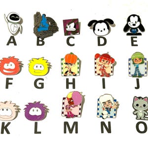 May include: A collection of colorful enamel pins featuring various cartoon characters. The pins include characters like Wall-E, a dog, and a cat. Each pin is a different shape and color, with a shiny finish.