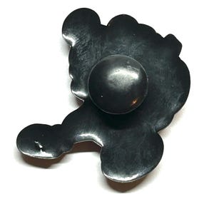 K&ouml;nnte beinhalten: Ein schwarzer Metall-Schrankknopf mit abgerundeter Mitte und dekorativer, stilisierter Form. Der Knopf hat eine matte Oberfl&auml;che und ist vor einem wei&szlig;en Hintergrund platziert. Das Design erinnert an eine Blume oder eine abstrakte Form.