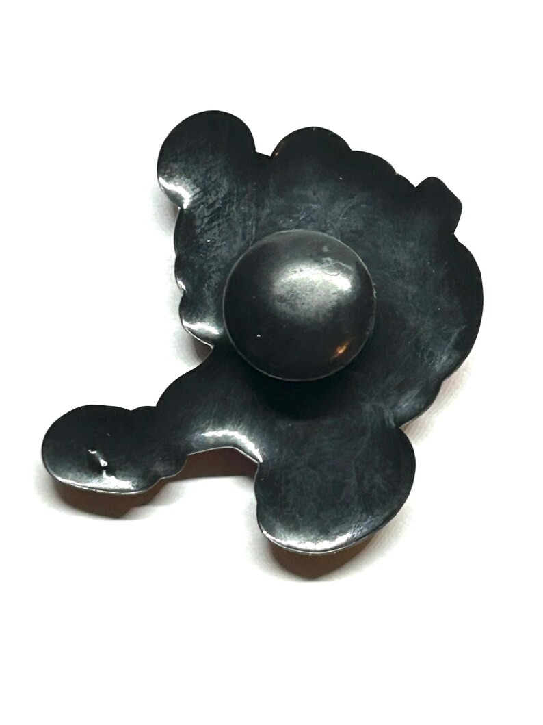 K&ouml;nnte beinhalten: Ein schwarzer Metall-Schrankknopf mit abgerundeter Mitte und dekorativer, stilisierter Form. Der Knopf hat eine matte Oberfl&auml;che und ist vor einem wei&szlig;en Hintergrund platziert. Das Design erinnert an eine Blume oder eine abstrakte Form.