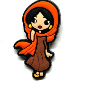 Puede incluir: Un dije de estilo caricatura que representa a una mujer con un vestido marr&oacute;n y un pa&ntilde;uelo naranja. El dije tiene contornos negros y pendientes amarillos. La mujer tiene el pelo negro y una expresi&oacute;n de sorpresa. El dije est&aacute; sobre un fondo blanco.