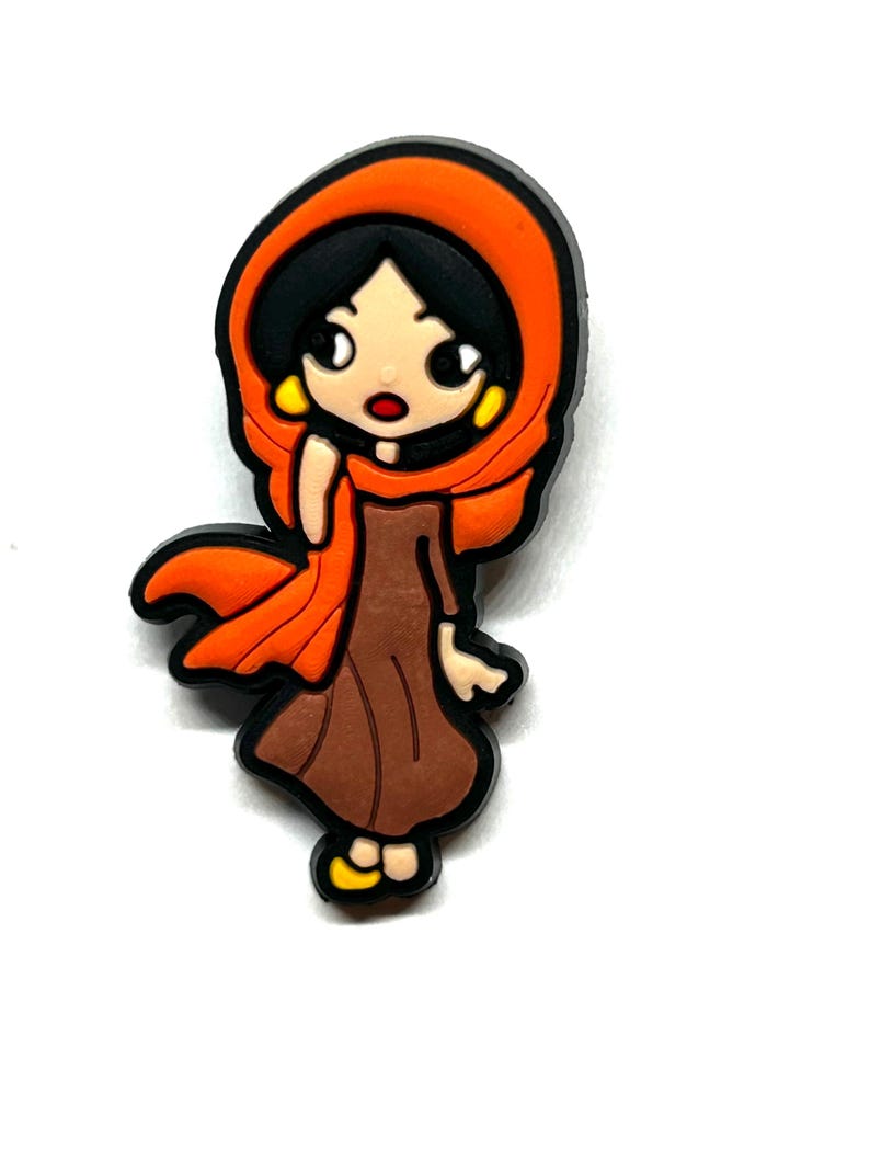 Puede incluir: Un dije de estilo caricatura que representa a una mujer con un vestido marr&oacute;n y un pa&ntilde;uelo naranja. El dije tiene contornos negros y pendientes amarillos. La mujer tiene el pelo negro y una expresi&oacute;n de sorpresa. El dije est&aacute; sobre un fondo blanco.