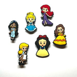 Puede incluir: Una colecci&oacute;n de coloridos dijes de personajes de dibujos animados, incluyendo a Jasmine, Cenicienta, Ariel, Bella y Blancanieves. Cada dije presenta un dise&ntilde;o detallado con colores vibrantes y probablemente est&aacute; hecho de goma o un material similar.