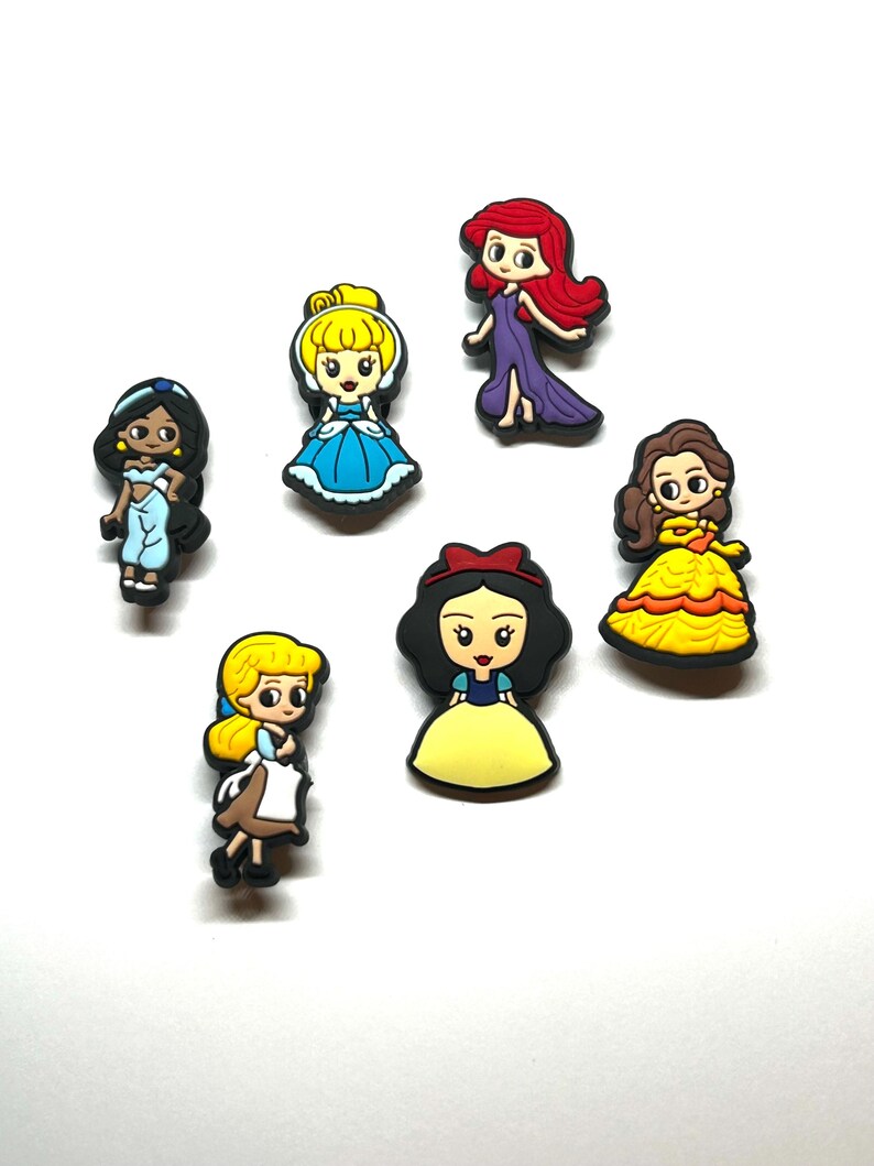 Puede incluir: Una colecci&oacute;n de coloridos dijes de personajes de dibujos animados, incluyendo a Jasmine, Cenicienta, Ariel, Bella y Blancanieves. Cada dije presenta un dise&ntilde;o detallado con colores vibrantes y probablemente est&aacute; hecho de goma o un material similar.