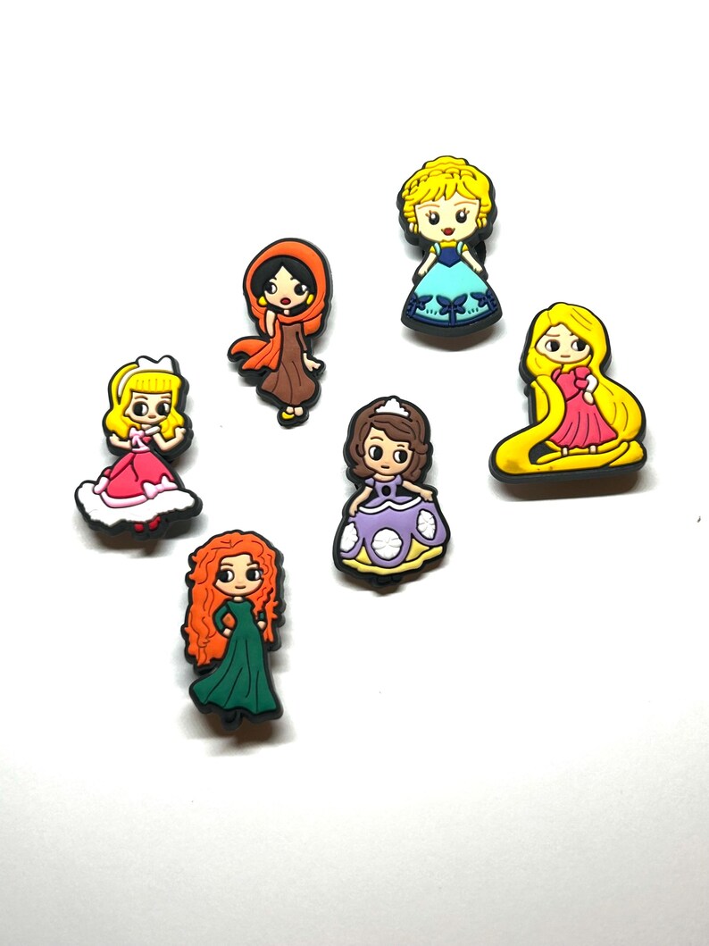 Puede incluir: Una colecci&oacute;n de amuletos de personajes de dibujos animados coloridos, con varias princesas con diferentes atuendos. Los amuletos est&aacute;n hechos de un material brillante y est&aacute;n sobre un fondo blanco. Cada amuleto tiene un dise&ntilde;o y una combinaci&oacute;n de colores &uacute;nicos.