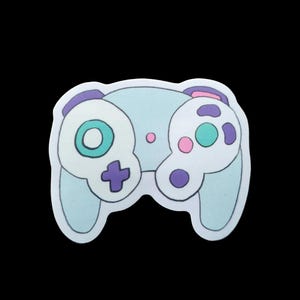 May include: A light blue sticker of a video game controller with white, purple, pink, and teal accents. The controller has a cross-shaped directional pad, two analog sticks, and several buttons. The sticker is on a black background.