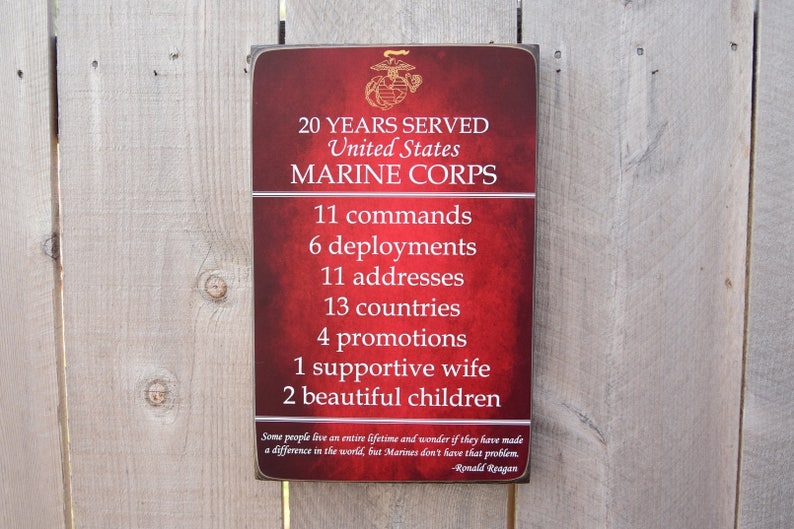 May include: A red wooden sign with a gold United States Marine Corps emblem. The sign lists 20 years of service, 11 commands, 6 deployments, 11 addresses, 13 countries, 4 promotions, 1 supportive wife, and 2 beautiful children. The sign includes a quote by Ronald Reagan: "Some people live an entire lifetime and wonder if they have made a difference in the world, but Marines don't have that problem."