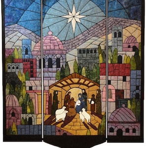 Può includere: Un arazzo da parete trapuntato in stile vetrata che rappresenta la scena della Natività. La scena include una stella, una stalla, una mangiatoia, un bambino, Maria, Giuseppe, pastori e pecore. Lo sfondo è una città con un cielo blu.