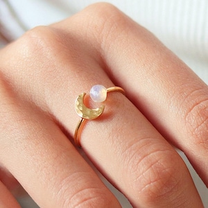May include: Gold ring with a hammered crescent moon design and a white opal gemstone.