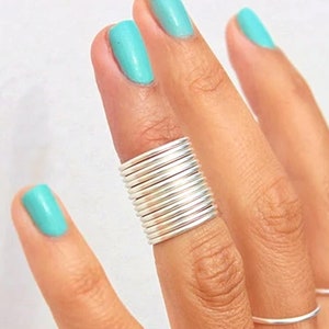 Può includere: Un anello d'argento fatto di bande impilate. L'anello è indossato sull'indice di una mano con smalto per unghie turchese.