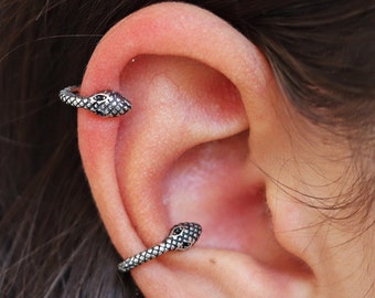 May include: Three silver snake ear cuffs with black detailing. The snake heads are facing forward. The cuffs are worn on the upper ear, helix, and lobe.