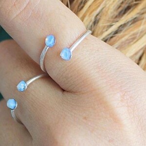 Könnte beinhalten: Ein silberner Ring mit drei hellblauen Edelsteinen. Der Ring ist verstellbar und kann an verschiedenen Fingern getragen werden.
