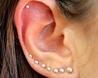 May include: Close-up of a person's ear with multiple silver stud earrings. The earrings are arranged in a line, starting at the top of the ear and going down to the lobe. The earrings are all different sizes, with the largest one at the bottom.