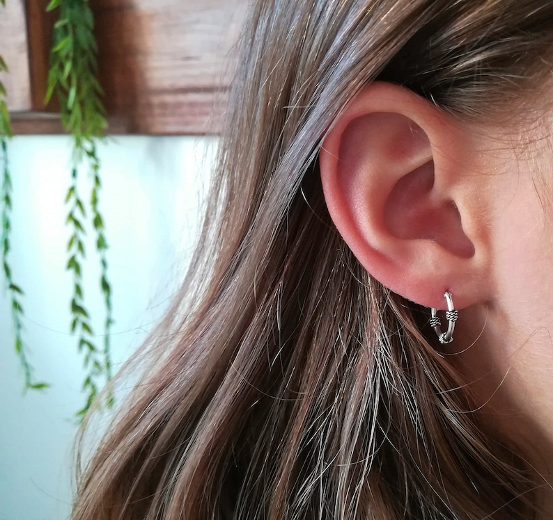 May include: Silver hoop earrings with a textured design. The earrings are worn in the earlobe.