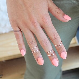 May include: A hand wearing several thin silver rings on the fingers. The nails are painted a light pink color.