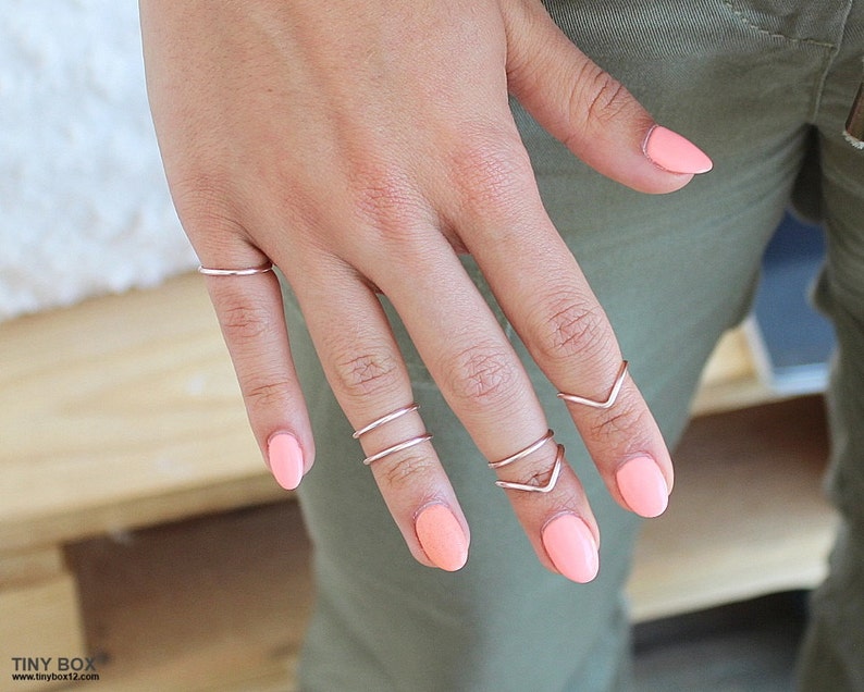 May include: A hand wearing several thin silver rings on the fingers. The nails are painted a light pink color.