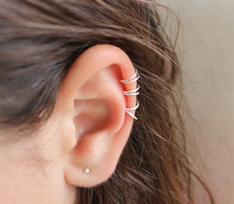 Pu&ograve; includere: Gioielli per orecchie a forma di manicotto in argento con pi&ugrave; anelli impilati sulla parte superiore dell'orecchio. Il manicotto per orecchie &egrave; indossato sull'orecchio sinistro.