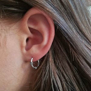 May include: A close-up of a person's ear with a small silver hoop earring. The earring has a textured design.