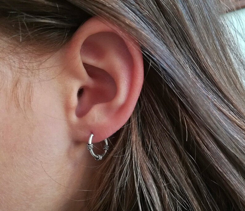 May include: A close-up of a person's ear with a small silver hoop earring. The earring has a textured design.