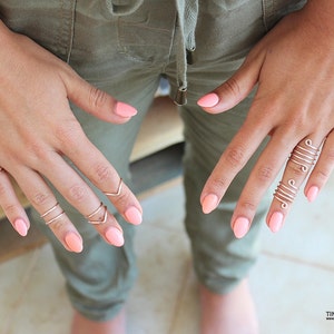 May include: Close-up of hands wearing multiple silver rings on several fingers. The rings are thin and delicate, with some featuring a simple spiral design. The nails are painted a light pink color.