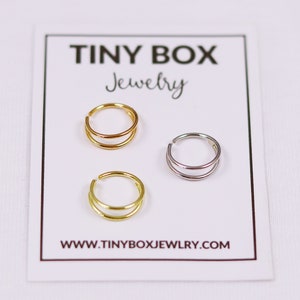 Pu&ograve; includere: Tre orecchini a cerchio doppio in oro, argento e oro rosa. Gli orecchini sono esposti su una carta bianca con il testo "TINY BOX Jewelry" e "www.tinyboxjewelry.com".