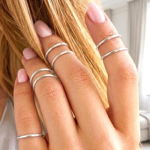 Peut inclure: Gros plan de plusieurs bagues en argent portées aux doigts. Les bagues sont fines et minimalistes, avec un design simple et élégant. Les doigts ont un teint clair et sont ornés des bagues, créant un look délicat et élégant. L'arrière-plan est flou.