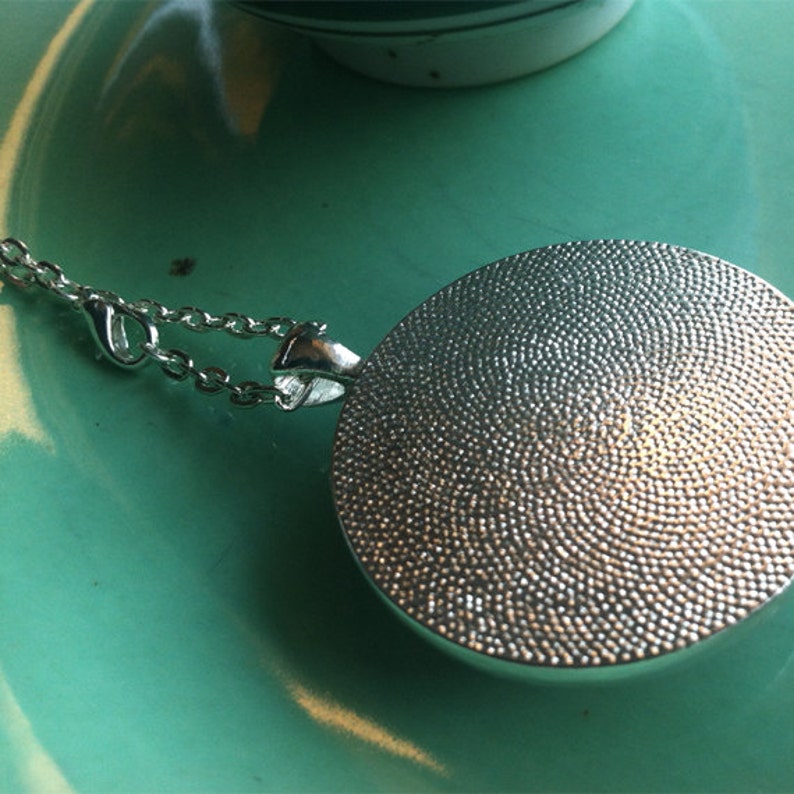 May include: A silver necklace with a round pendant. The pendant has a textured surface and a silver chain.