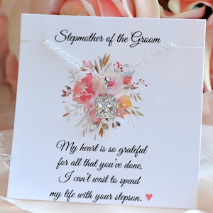 May include: A white card with the text 'Stepmother of the Groom' printed on it. The card has a floral design with pink and orange flowers. A silver necklace with a square-shaped pendant is displayed on the card. The text on the card reads: 'My heart is so grateful for all that you've done, I can't wait to spend my life with your stepson.' The text 'So Blessed Designs' is printed in the bottom right corner of the card.