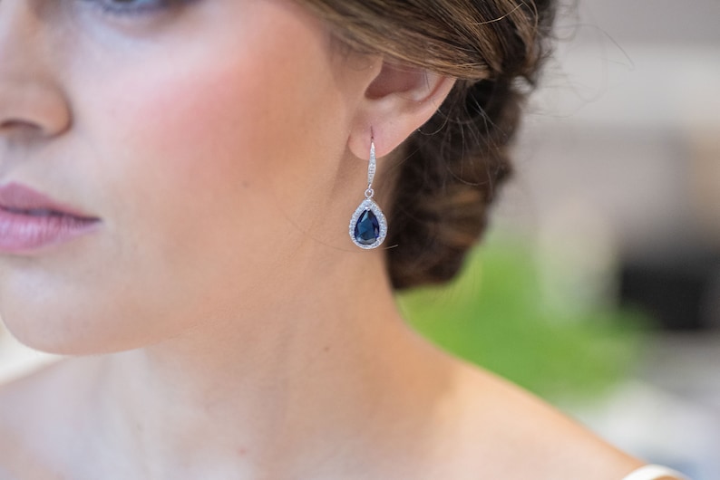 May include: A pair of silver teardrop earrings with a dark blue gemstone surrounded by smaller clear gemstones.