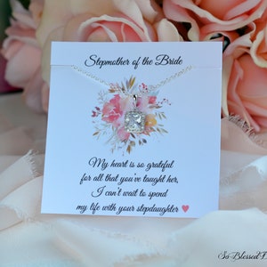 May include: A silver necklace with a square clear crystal pendant on a white card with the text "Stepmother of the Bride" and a message about being grateful for all that the stepmother has taught the bride. The card also includes the text "So Blessed Designs".