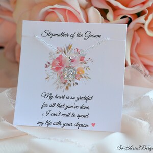 May include: A silver necklace with a square-shaped clear crystal pendant on a white card with the text "Stepmother of the Groom" and a message about being grateful for all that has been done and looking forward to spending life with the stepson.