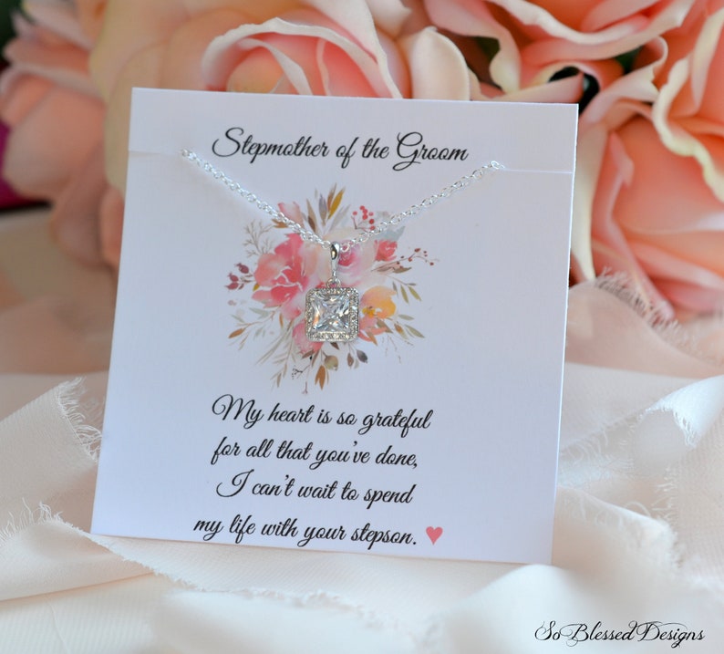 May include: A silver necklace with a square-shaped clear crystal pendant on a white card with the text "Stepmother of the Groom" and a message about being grateful for all that has been done and looking forward to spending life with the stepson.