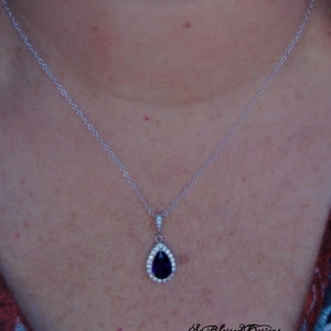 May include: A silver chain necklace with a teardrop-shaped pendant featuring a large, dark purple gemstone surrounded by smaller clear gemstones.