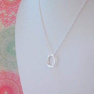 Pu&ograve; includere: Una collana d'argento con un ciondolo a doppio anello. La collana &egrave; su un manichino bianco.