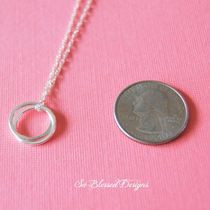 Pu&ograve; includere: Collana d'argento con ciondolo a doppio anello. Il ciondolo &egrave; circa delle dimensioni di una moneta da 25 centesimi di dollaro americano.