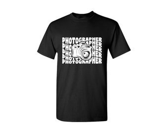 May include: Black t-shirt with a white graphic of a camera and the word "PHOTOGRAPHER" repeated in a pattern.