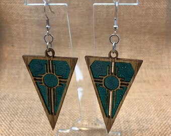 Könnte beinhalten: Ein Paar Holzohrringe mit einem türkisfarbenen und braunen geometrischen Design. Die Ohrringe sind dreieckig geformt und haben ein indianisches Symbol in der Mitte.