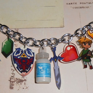 Pode incluir: Um bracelete de corrente de prata com pingentes que representam personagens e itens da série de videogames The Legend of Zelda. Os pingentes incluem um coração, uma espada, uma chave, um escudo, uma garrafa, uma funda, uma gema verde e um personagem do jogo.