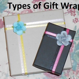 May include: Two gift boxes wrapped in different styles. One box is wrapped in brown paper with yellow and white ribbon and a light blue flower. The other box is wrapped in black paper with pink and black ribbon and a gray flower.