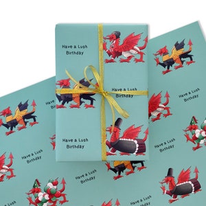 Könnte beinhalten: Blaues Geschenkpapier mit einem sich wiederholenden Muster aus roten und gelben Drachen. Das Papier trägt den Text "Have a Lush Birthday", der sich über die gesamte Fläche wiederholt.