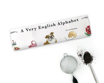 May include: A white tea towel with the text "A Very English Alphabet" and an illustration of a bulldog, a teapot, a cake stand, a biscuit, and a rose. The text "D is for Dunking" is also included.