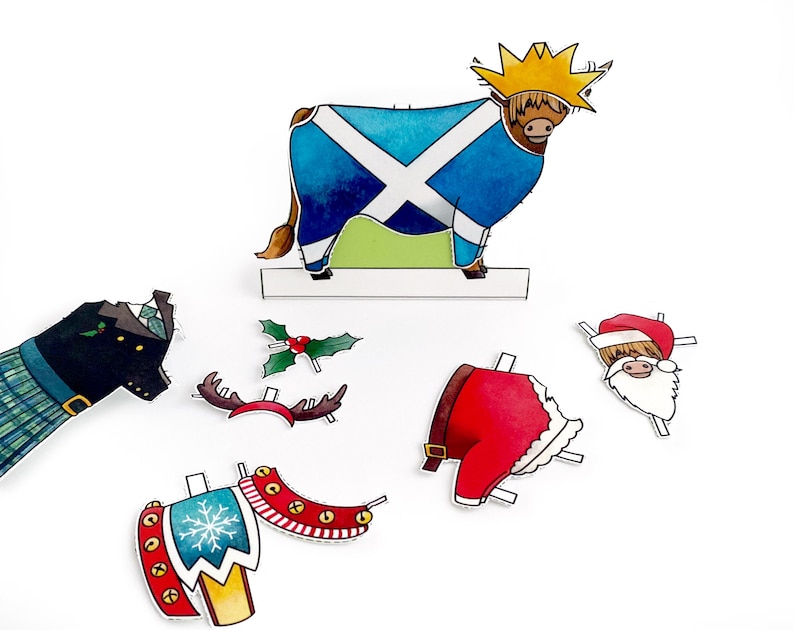 May include: A set of paper craft cutouts featuring a Scottish Highland cow, a Father Christmas, a reindeer, a Christmas tree, and a Scottish kilt. The cutouts are printed on white paper with colourful details.