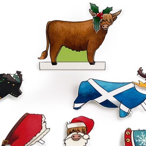 May include: A set of Christmas-themed paper cutouts featuring a Highland cow wearing a holly wreath, a Santa Claus, a Scottish flag, a kilt, a Christmas stocking, and a reindeer antler headband.