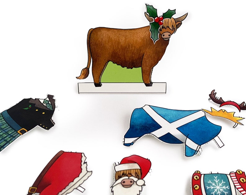 May include: A set of Christmas-themed paper cutouts featuring a Highland cow wearing a holly wreath, a Santa Claus, a Scottish flag, a kilt, a Christmas stocking, and a reindeer antler headband.