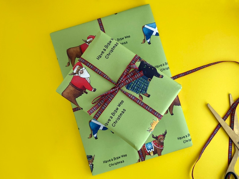 May include: Green wrapping paper with a Scottish Highland cow design. The paper features the text "Have a Braw Wee Christmas" repeated throughout. The paper is tied with a red and black tartan ribbon.