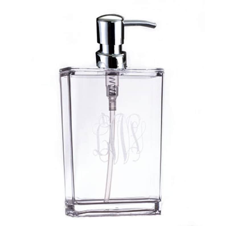 May include: A clear acrylic soap dispenser with a silver pump and a monogrammed design. The monogram is the letters "GMS" in a script font.