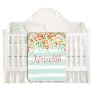 May include: A mint green and white striped baby blanket with a floral design and the name "Meredith" in pink lettering.