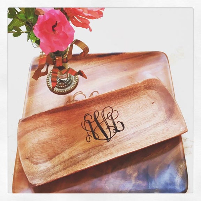 May include: Two wooden serving trays, one rectangular and one oval, with a monogrammed design. The oval tray has the initials "LLL" in a cursive font. The trays are made of natural wood and have a warm brown color.