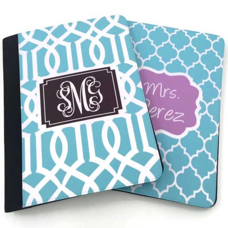 K&ouml;nnte beinhalten: Zwei blaue und wei&szlig;e gemusterte Notizbuchh&uuml;llen. Eine H&uuml;lle hat ein Monogramm "S.M.G." in einem braunen Rechteck. Die andere H&uuml;lle hat ein violettes Rechteck mit dem Text "Frau Perez".